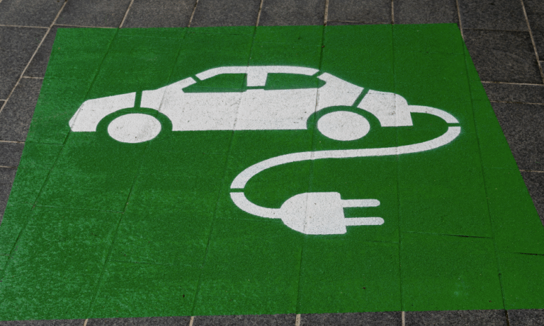 UM desenho no chão mostrando um carro do qual sai um fio de tomada, representando um carro elétrico.