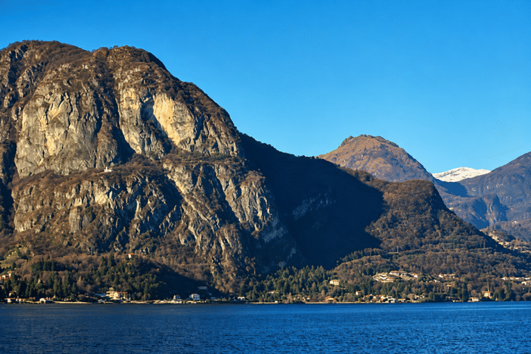 Montanhas rochosas às margens de um lago azul, com vegetação e céu limpo.